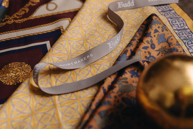 Gold bauble laid across gold and yellow patterned silk pocket squares and scarves
