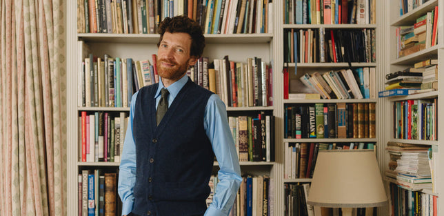 Man stood in library wearing a business shirt, tie and knitted vest