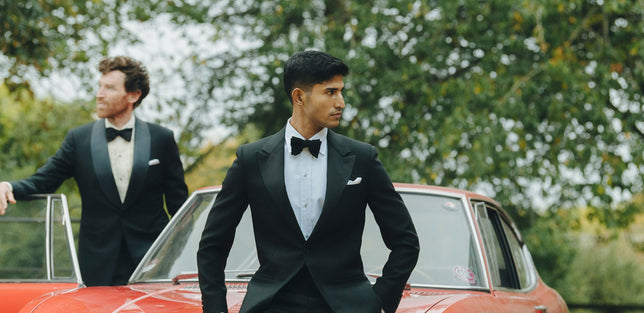 Two men wearing black tie stood infront of red car