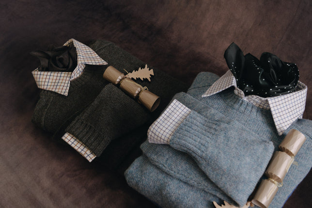 Two sweaters laid flat with shirts inside and gold christmas crackers on top