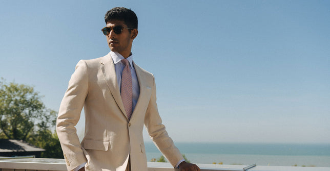 Man stood against beach and blue sky in beige lounge suit