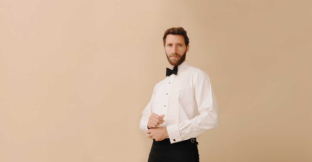 Model wearing white pleated dress shirt with black tie against cream plain background