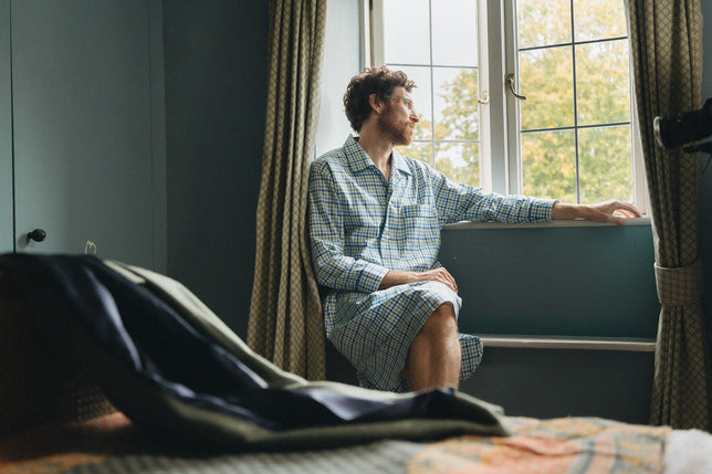 Man wearing checked nightshirt sat in window seat looking out of window