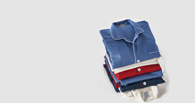 Stack of multi coloured mens pyjamas on plain pale grey background