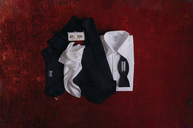 Black tie shirt and accessories laid out on red velvet background
