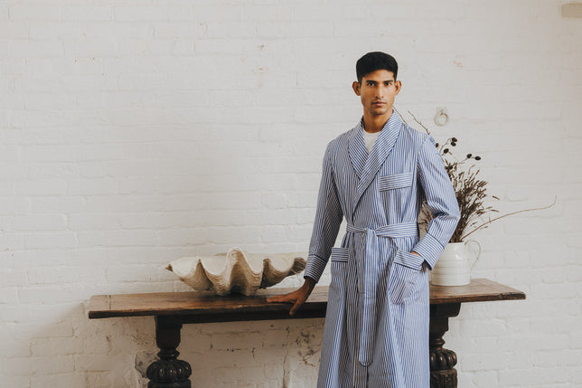 Man stood in Budd stripe blue dressing gown against white brick wall