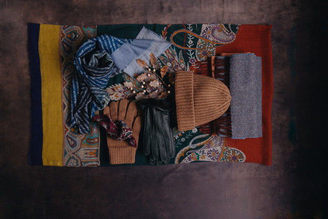 Selection of winter accessories, hats, gloves and scarves laid out with gold holly 