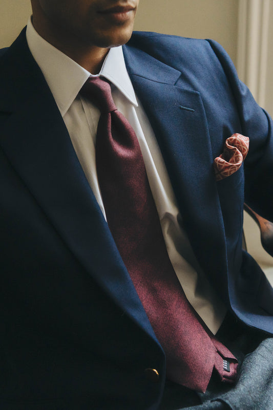 Man sat in chair wearing a navy business suit and close up of a dark red tie