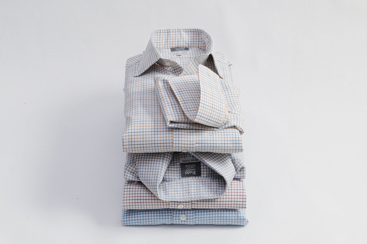 Stack of folded dress shirts with different patterns on a light gray background