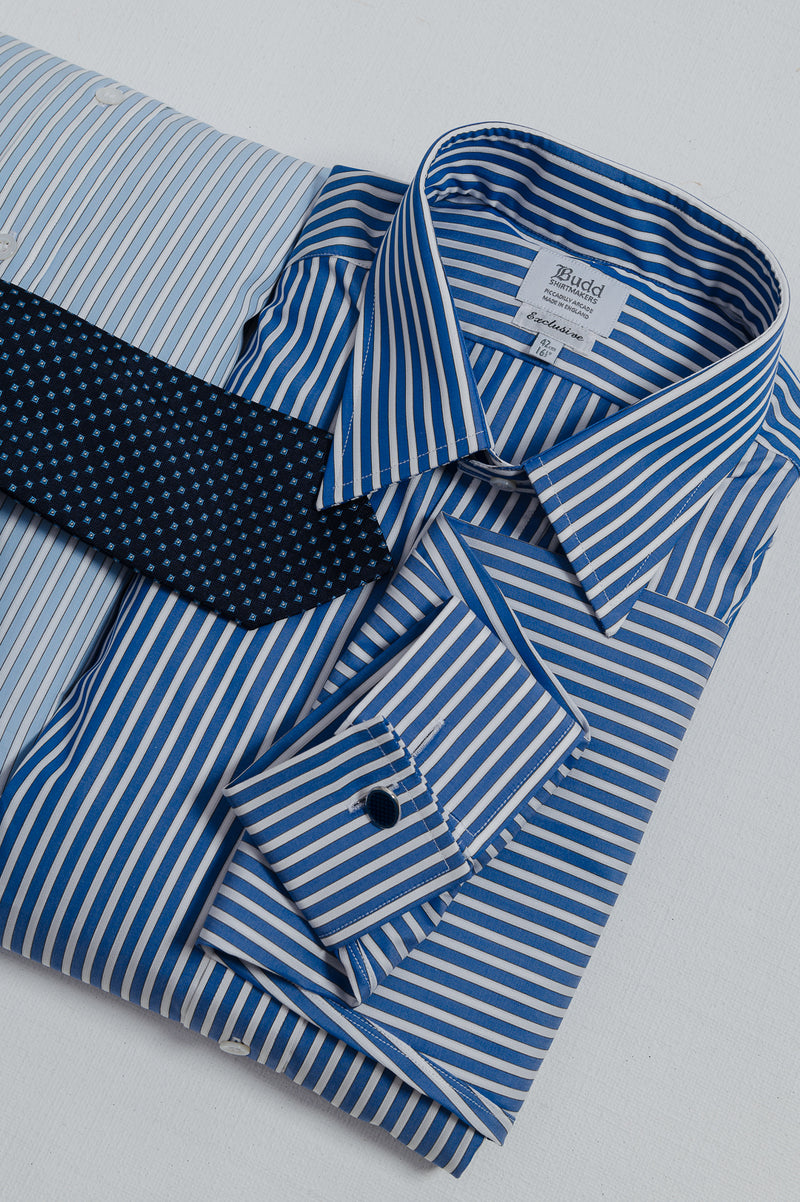 A folded blue and white striped dress shirt with a matching necktie, displayed on a light gray background. The brand name 'Budd' is visible on the inner collar label.