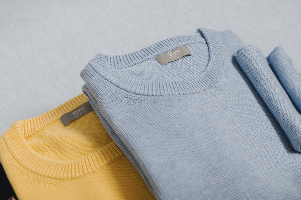 Two folded sweaters, one yellow and one blue, on a light gray background.