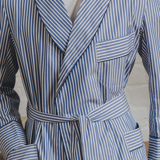 Detail shot of male model wearing blue stripe dressing gown stood against white brick background