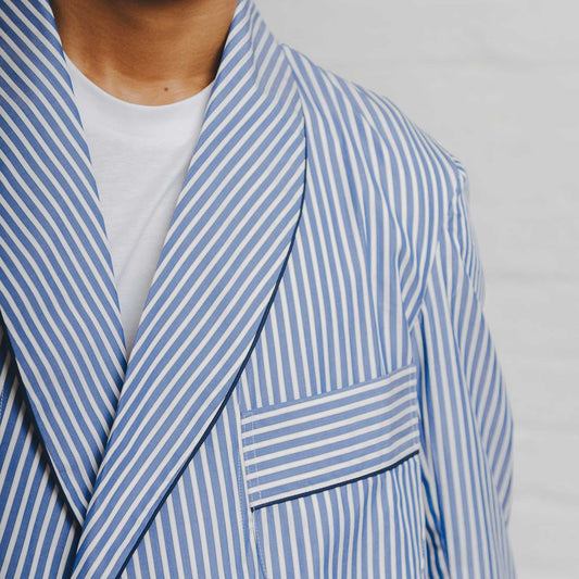 Male model wearing blue stripe dressing gown stood against white brick background