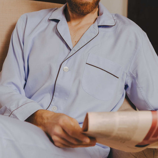 Man in light blue pajamas holding a newspaper on a couch.