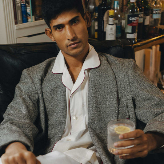 Man in a gray dressing gown and white pyjamas holding a drink with a lemon slice in a bar setting