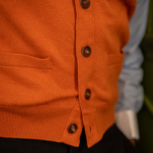 Detail of horn buttons and lower pockets on cashmere sleeveless cardigan in orange