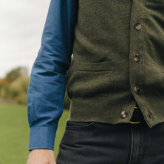 Person wearing a green vest over a blue shirt with a blurred outdoor background