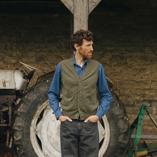 Man standing in front of a tractor wearing a green vest and blue shirt.