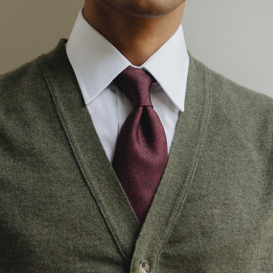 Man wearing a green sweater vest over a white shirt with a burgundy tie against a neutral background