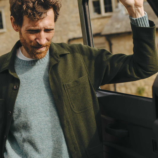 Man wearing a green chore jacket and blue jumper stood in door of car