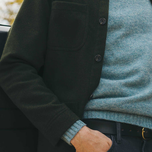 Close up of man wearing a green chore jacket and blue jumper stood in door of car