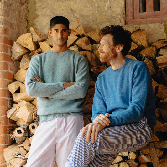 Two men wearing light blue sweaters in front of a stack of firewood.