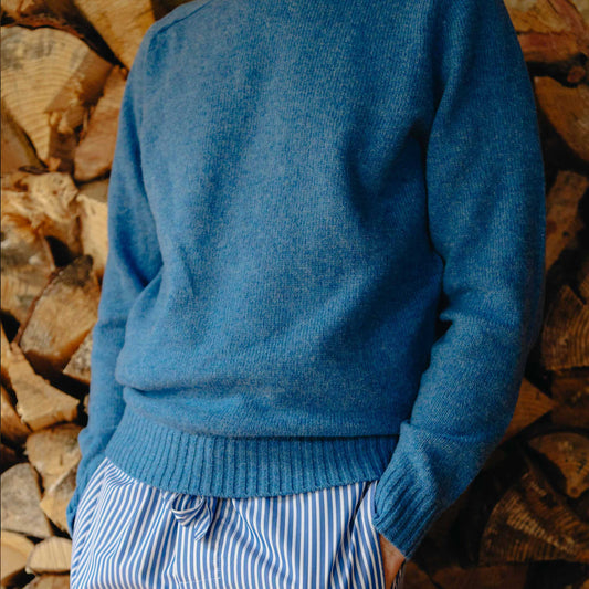 Person wearing a blue sweater and striped pants standing against a background of stacked logs.