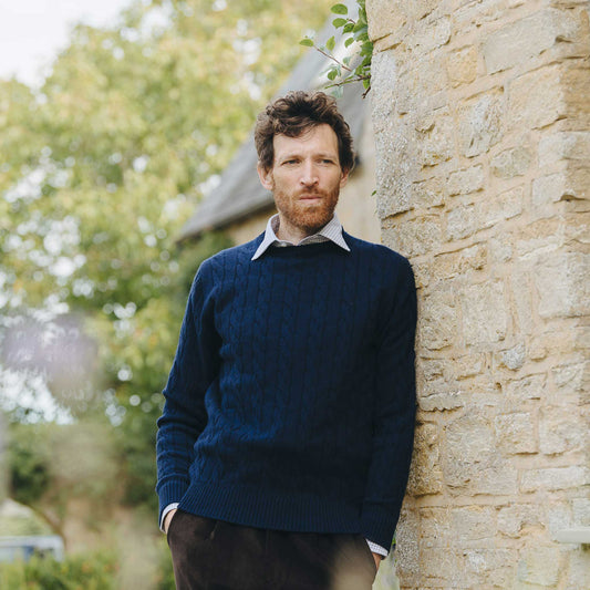 Man in a blue sweater leaning against a stone wall outdoors