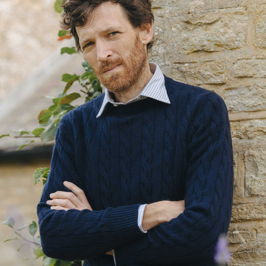 Man wearing a navy cable knit sweater against a stone wall.