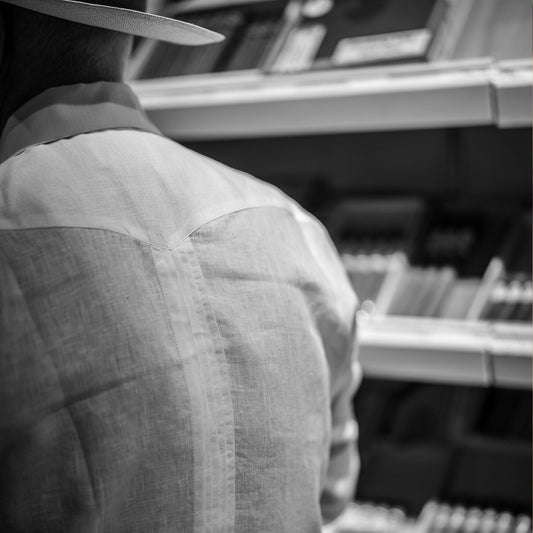 Person wearing a hat and light-colored shirt in a room with shelves and cigars