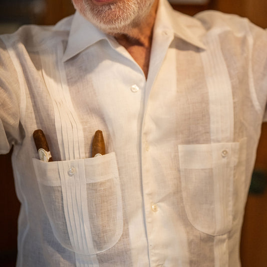 Man wearing a light-colored shirt with a pocket containing a cigar.