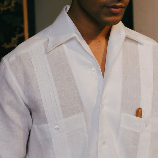 Close-up of a person wearing a light-colored, open-front shirt with a pocket and rolled-up sleeves.