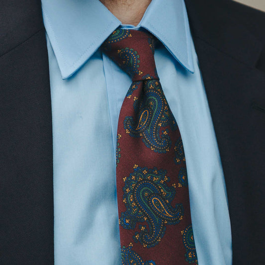 Close-up of a person wearing a blue dress shirt and a patterned red tie.