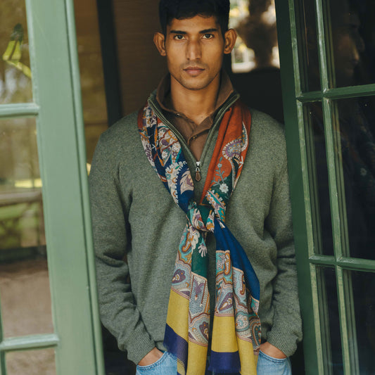 Man wearing a colorful scarf and gray sweater standing in front of a green door.