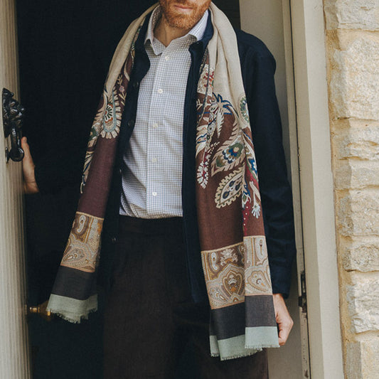 Man wearing a patterned scarf standing in front of a stone wall.