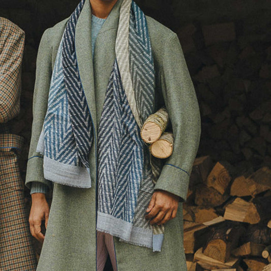 Person wearing a green coat and patterned scarf holding logs against a wooden background