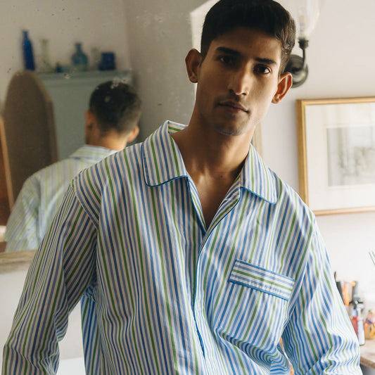 Man wearing a striped shirt standing in a room with a mirror and shelves.