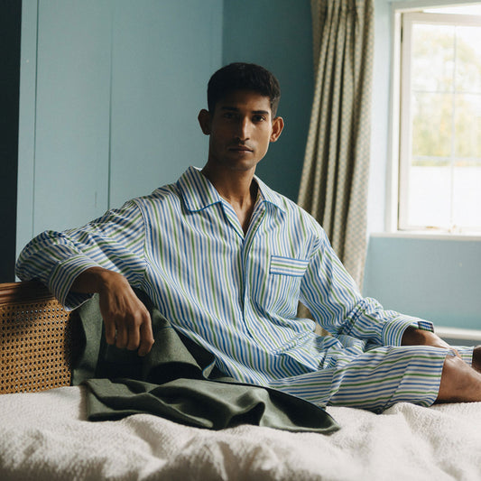Man wearing striped pajamas sitting on a bed in a room with a window and curtains.