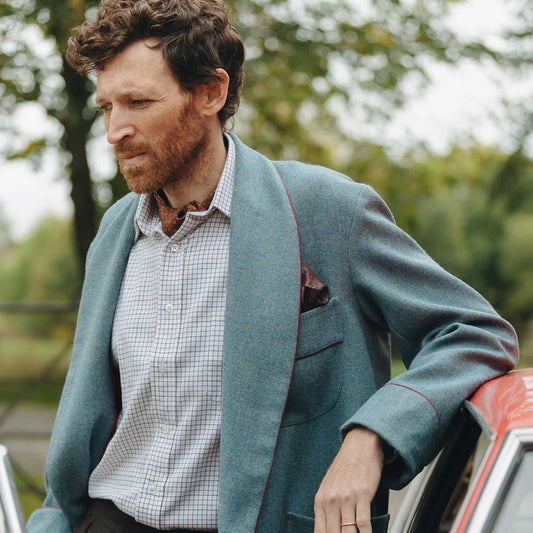 Detail shot of male model wearing a blue herringbone tweed dressing gown leant against vintage red car