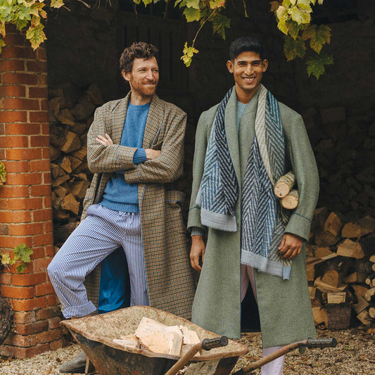 Two male models stood outside in log store wearing tweed dressing gowns and scarves