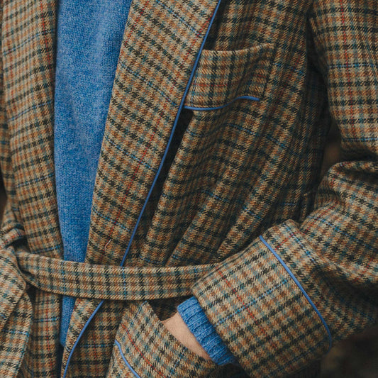 Male model stood with hands inside pockets wearing a brown checked dressing gown with blue sweater underneath