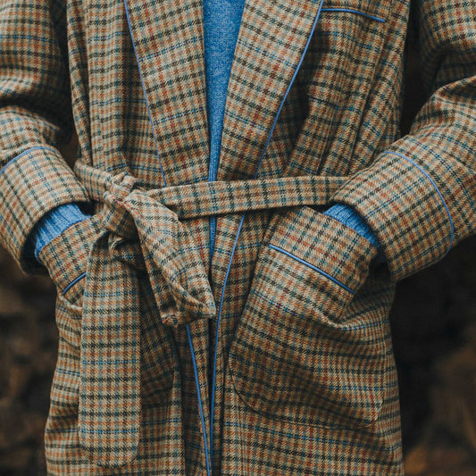 Male model stood with hands in pockets wearing a brown checked dressing gown with blue sweater underneath