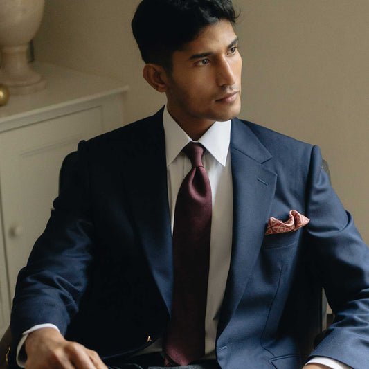 Close up of male sat in office wearing burgundy tie and navy suit jacket white shirt