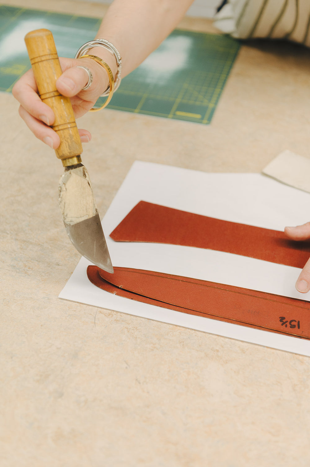 Person using a tool to cut a shirt pattern on a white surface with a green cutting mat in the background.
