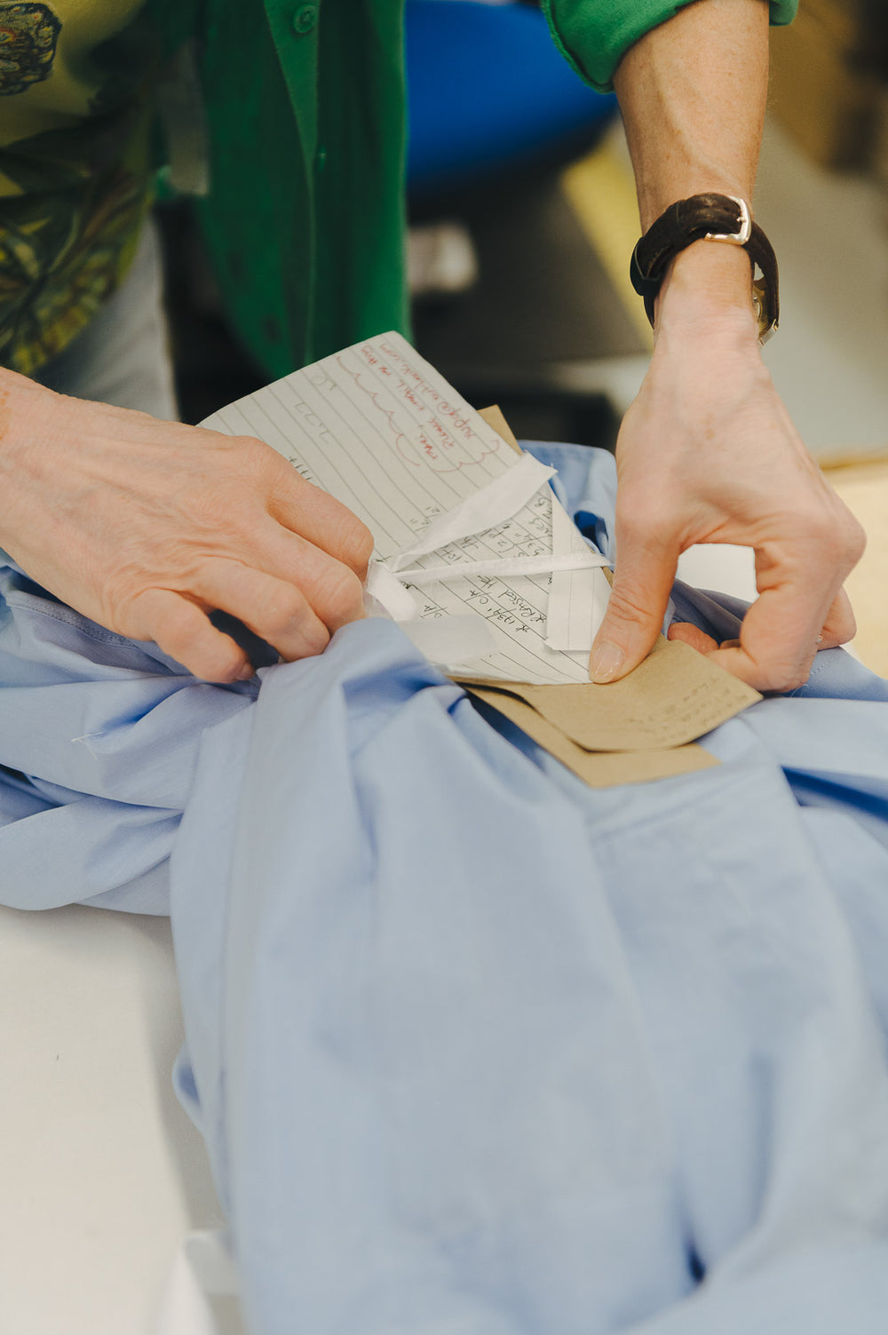 Person putting shirt fabric bundle with measurements on paper on a light blue garment