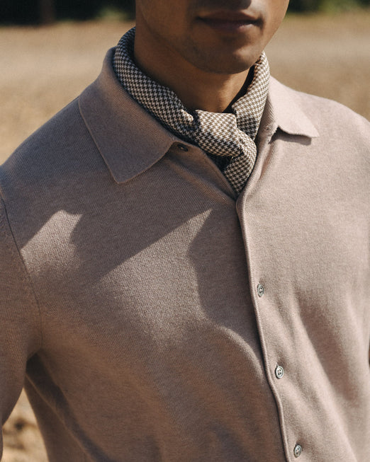 Man wearing a brown knitted shirt and checkered scarf outdoors