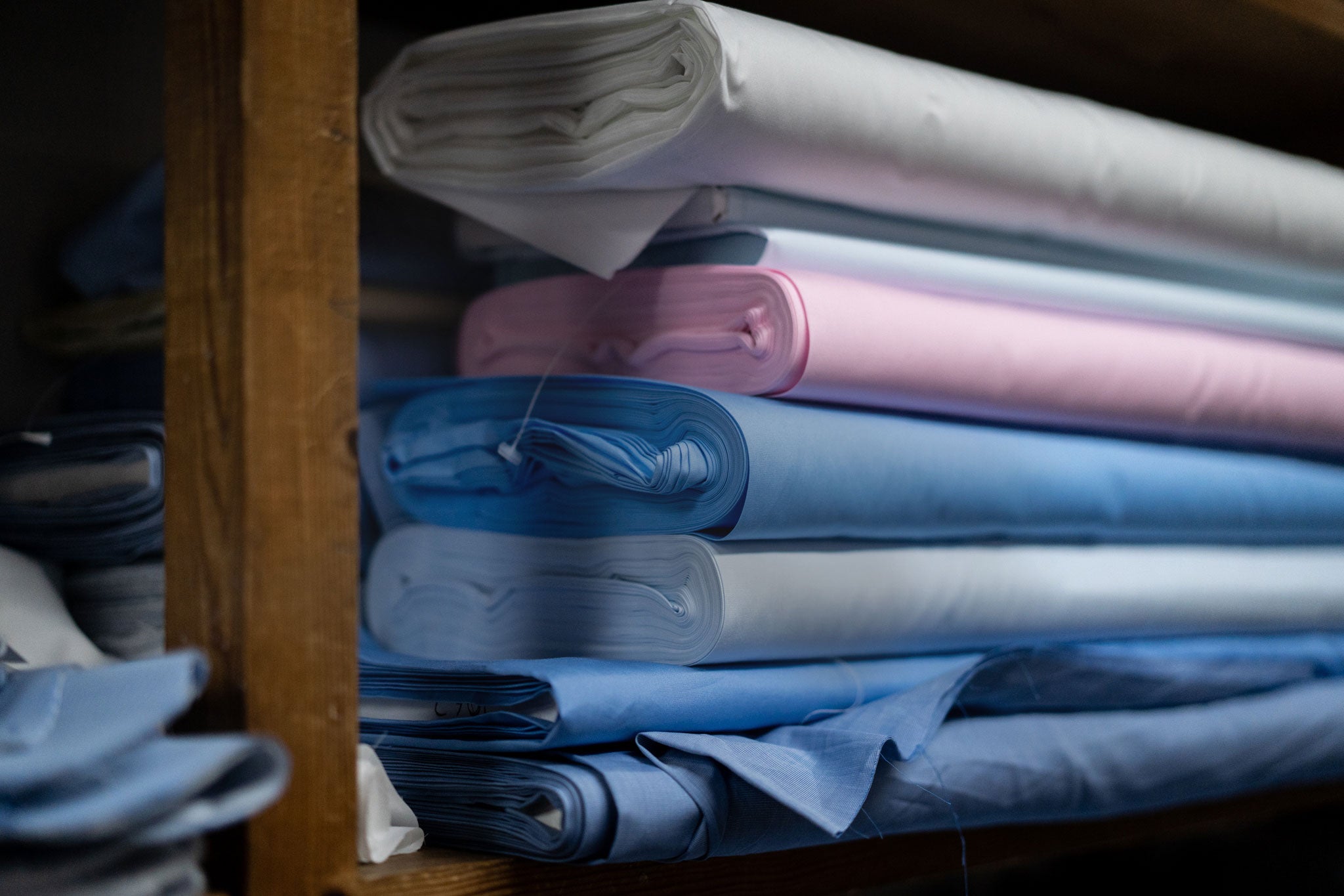 Stack of folded fabric in various colors on a wooden shelf.