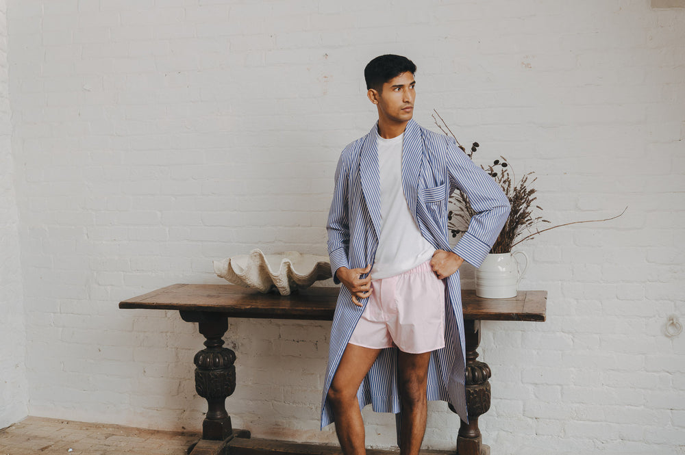 Man wearing pink boxer shorts with white t shirt and blue stripe dressing gown in a casual setting