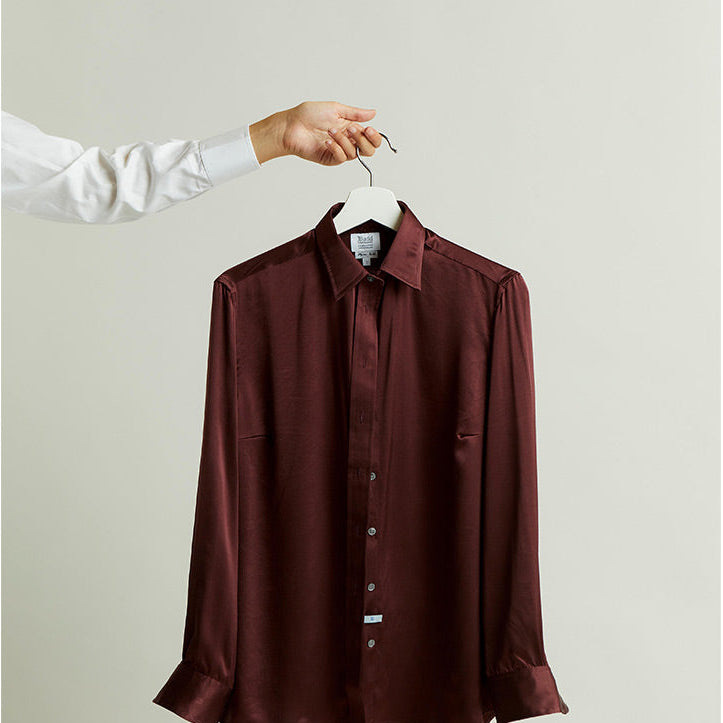 Claret red silk shirt on a hanger against a plain background