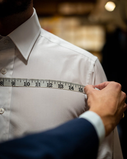 Person measuring a white shirt with a tape measure.